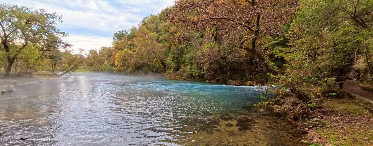 Eye-level 360 view beside the clear blue water of Big Spring under fall trees